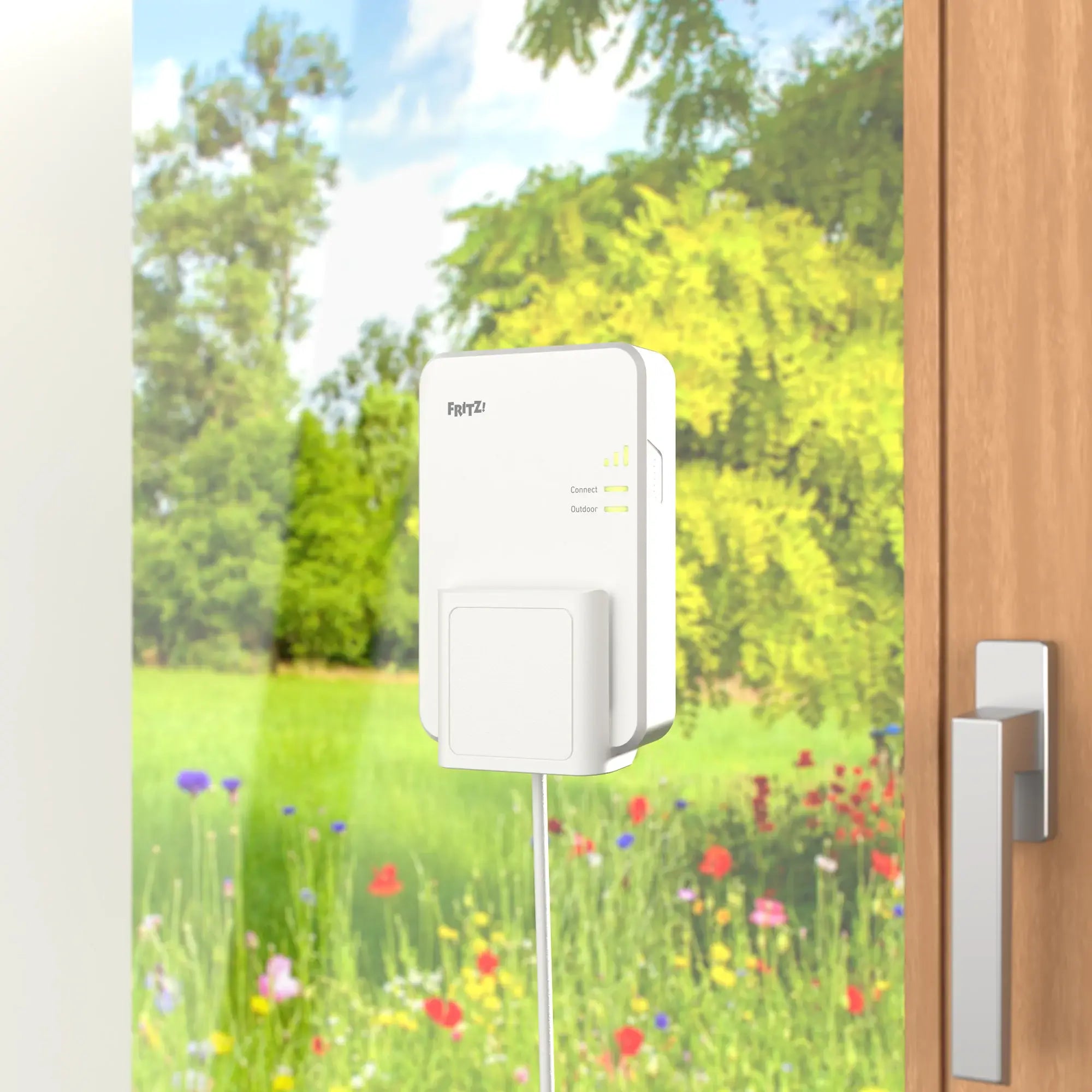 FRITZ!Repeater 1610 Outdoor montiert an einer Wand, mit buntem Garten im Hintergrund.